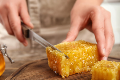 Photo of Woman cutting fresh honeycomb at table, closeup