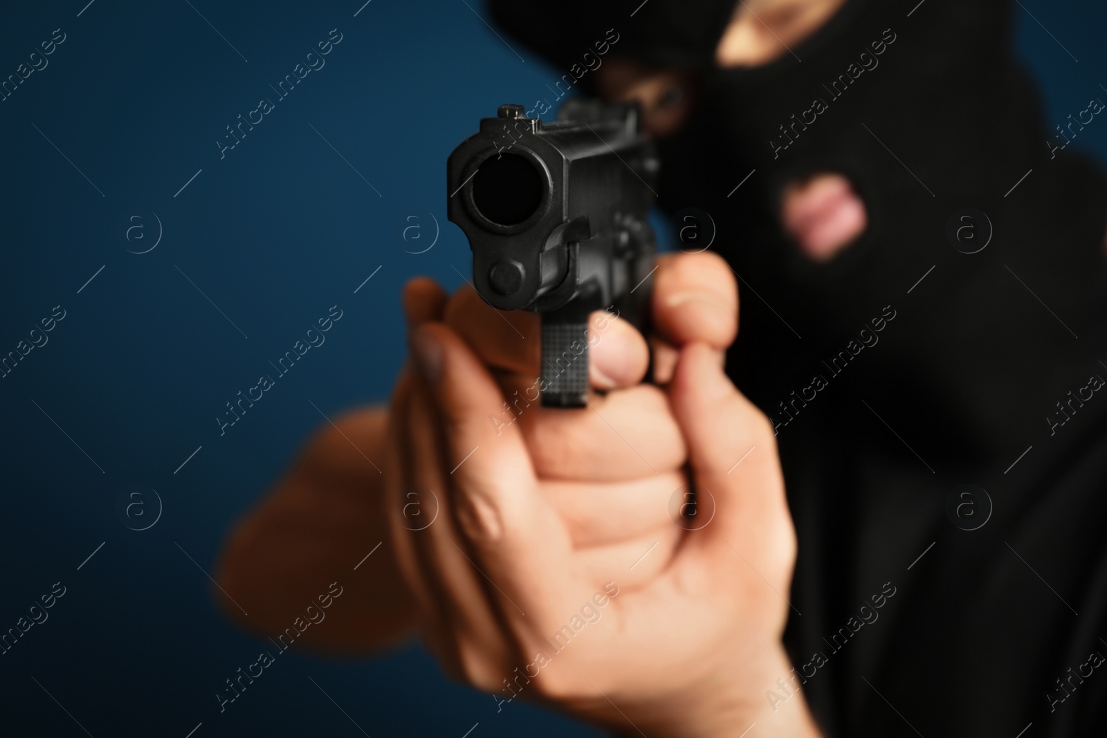 Photo of Man in mask holding gun against dark blue background, focus on hands