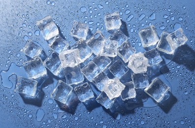 Photo of Melting ice cubes and water drops on blue background, flat lay