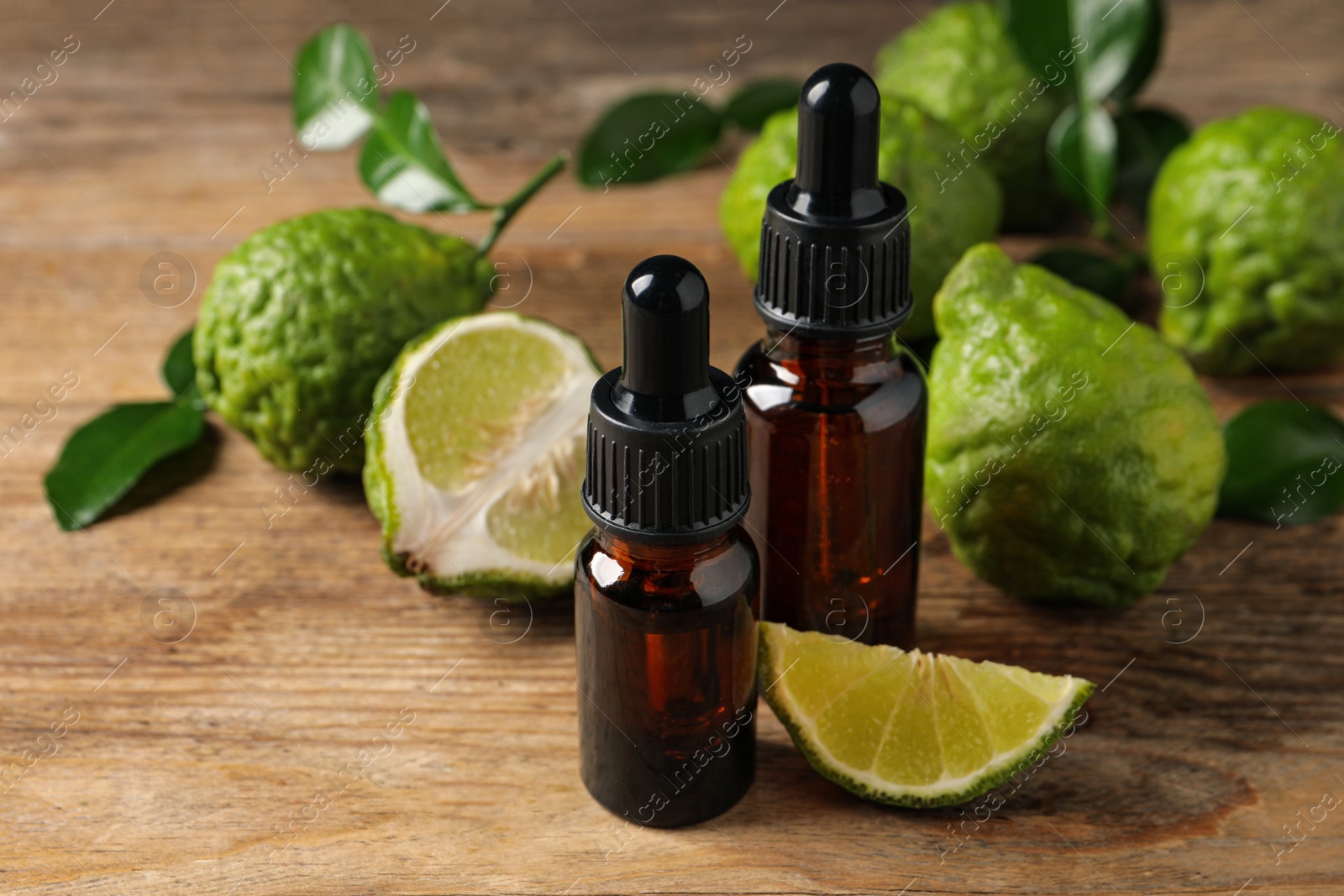 Photo of Bottles of essential oil and fresh bergamot fruits on wooden table