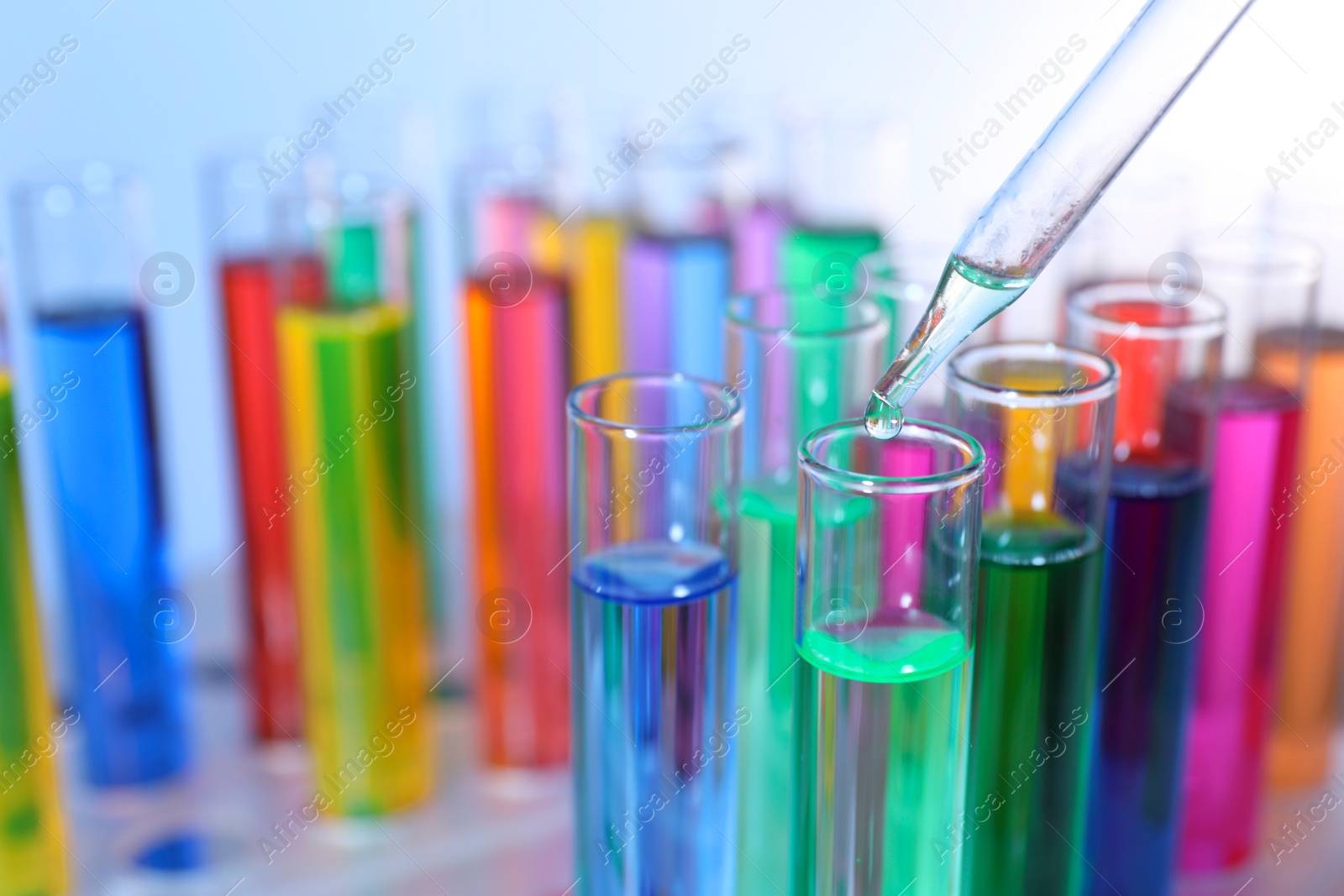 Photo of Dripping liquid from pipette into test tube on blurred background, closeup