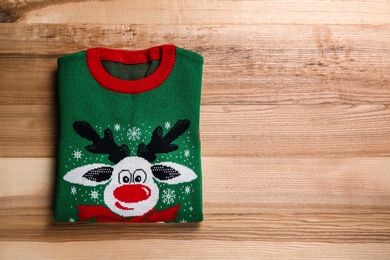 Folded warm Christmas sweater on wooden table, top view. Space for text