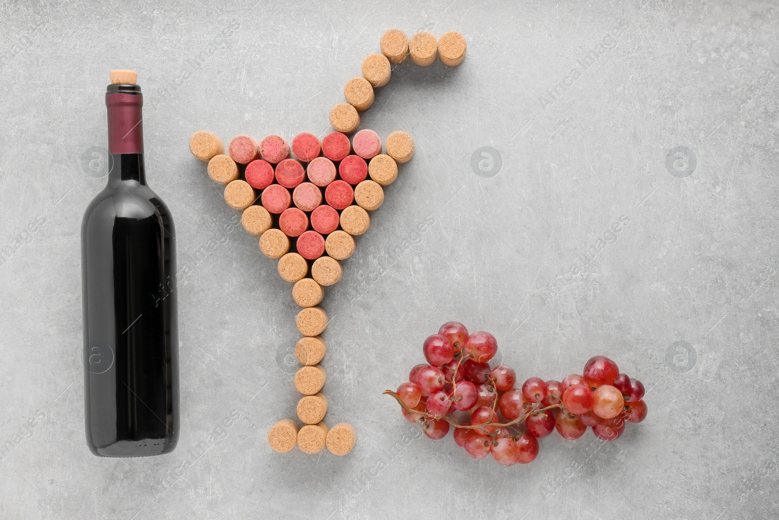 Photo of Cocktail glass with straw made of wine corks, bottle and grapes on light grey table, flat lay