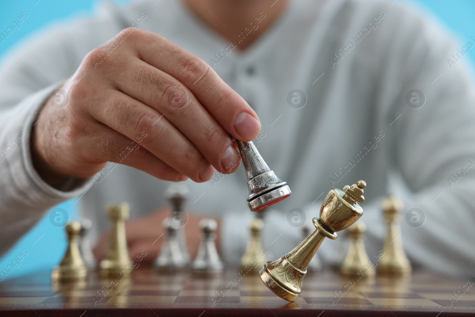 Photo of Man moving chess piece at checkerboard against light blue background, closeup