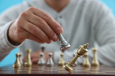 Man moving chess piece at checkerboard against light blue background, closeup