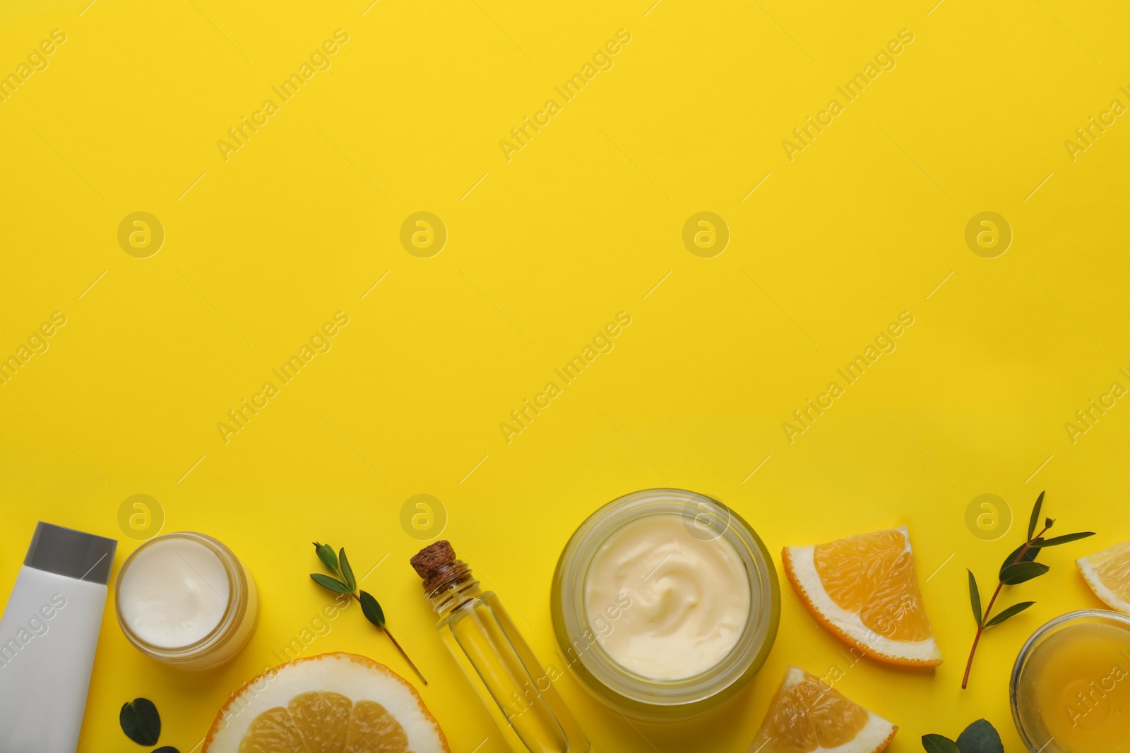 Photo of Body cream and other cosmetic products with ingredients on yellow background, flat lay. Space for text