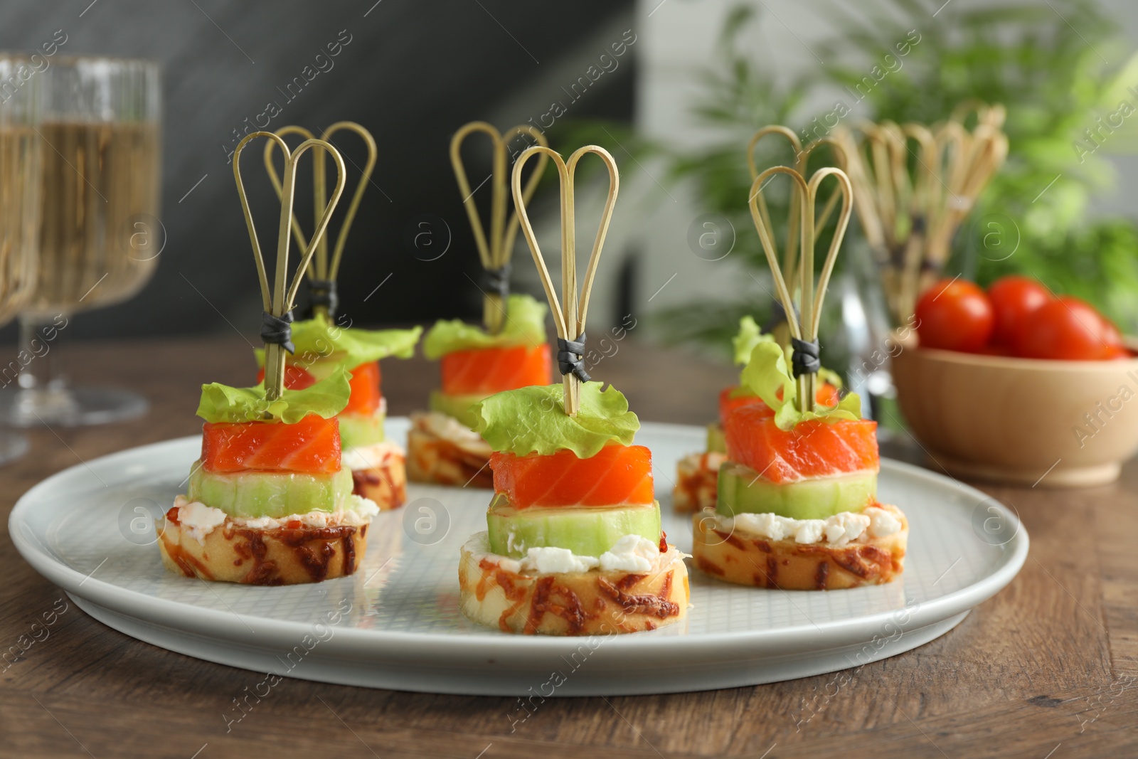 Photo of Tasty canapes with salmon, cucumber, bread and cream cheese on wooden table, closeup