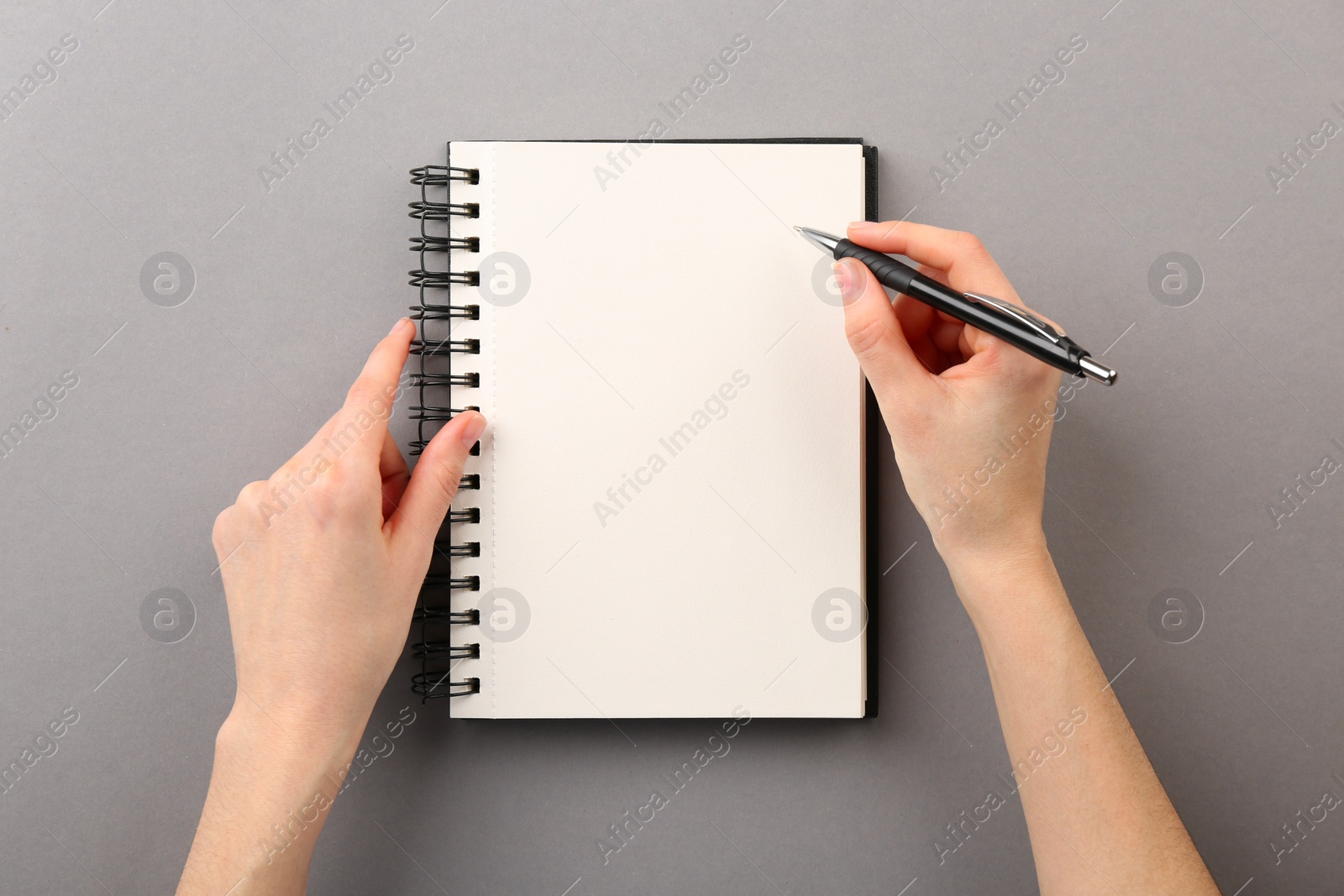 Photo of Woman writing in notebook on grey background, top view