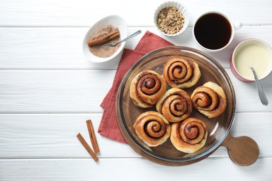 Photo of Tasty cinnamon rolls and ingredients on white wooden table, flat lay. Space for text