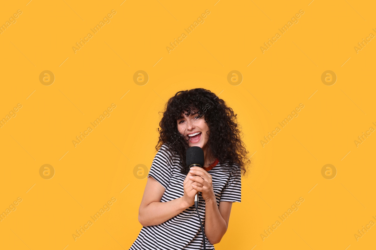 Photo of Beautiful young woman with microphone singing on yellow background