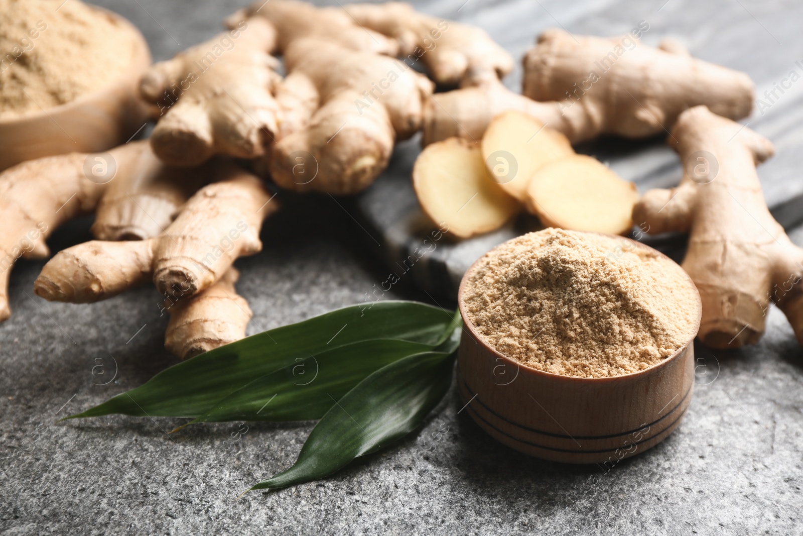 Photo of Dry ginger powder, fresh root and leaves on grey table