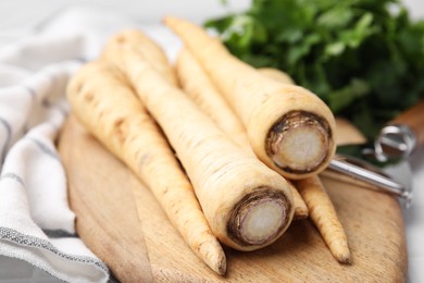 Photo of Raw parsley roots and peeler on table, closeup