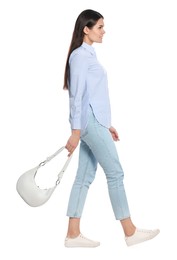 Young woman with handbag walking on white background