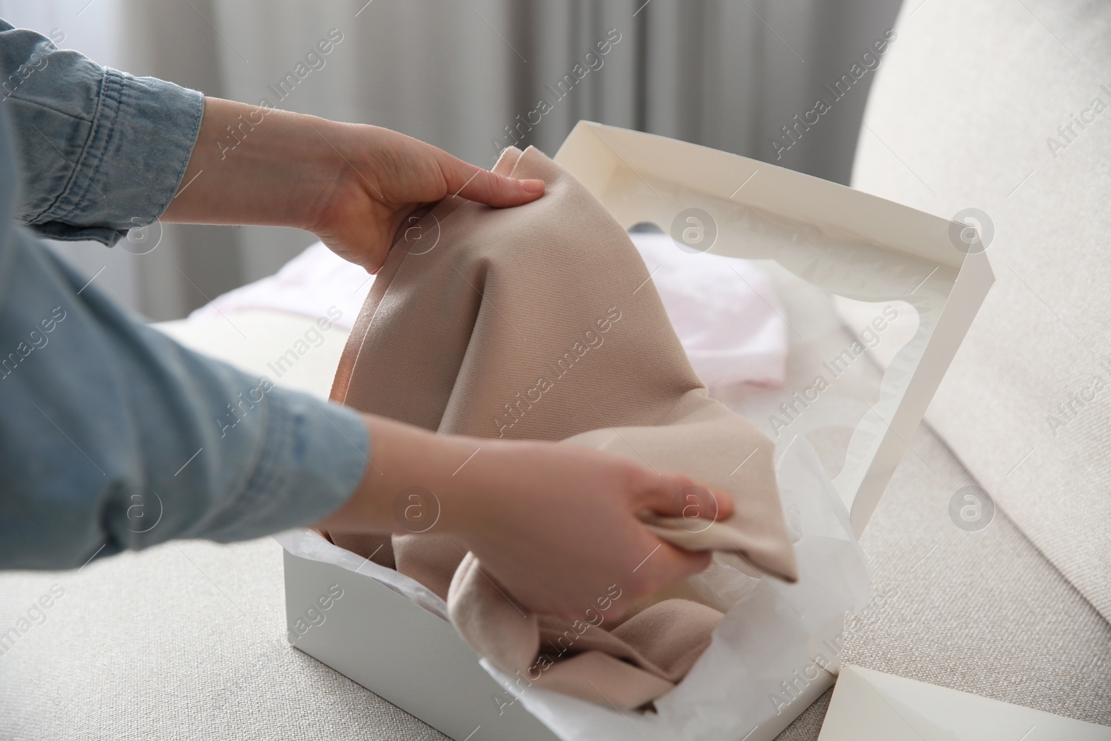 Photo of Woman taking soft cashmere sweater out of box indoors, closeup