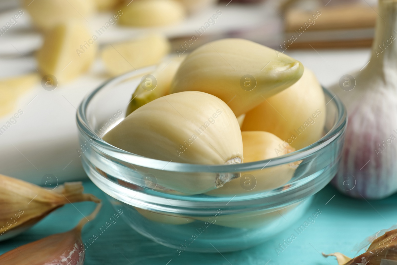 Photo of Fresh peeled garlic cloves in bowl on light blue wooden table, closeup. Organic product