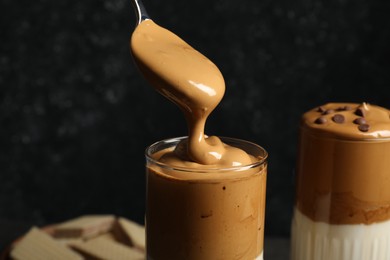 Photo of Pouring cream for dalgona coffee into glass on dark background, closeup