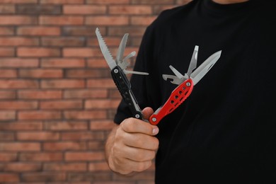 Man holding multitool near brick wall, closeup. Space for text