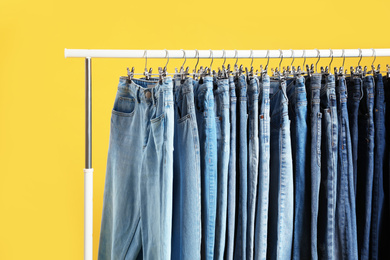 Rack with different jeans on yellow background