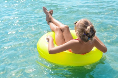 Photo of Little girl with inflatable ring in sea on sunny day, back view