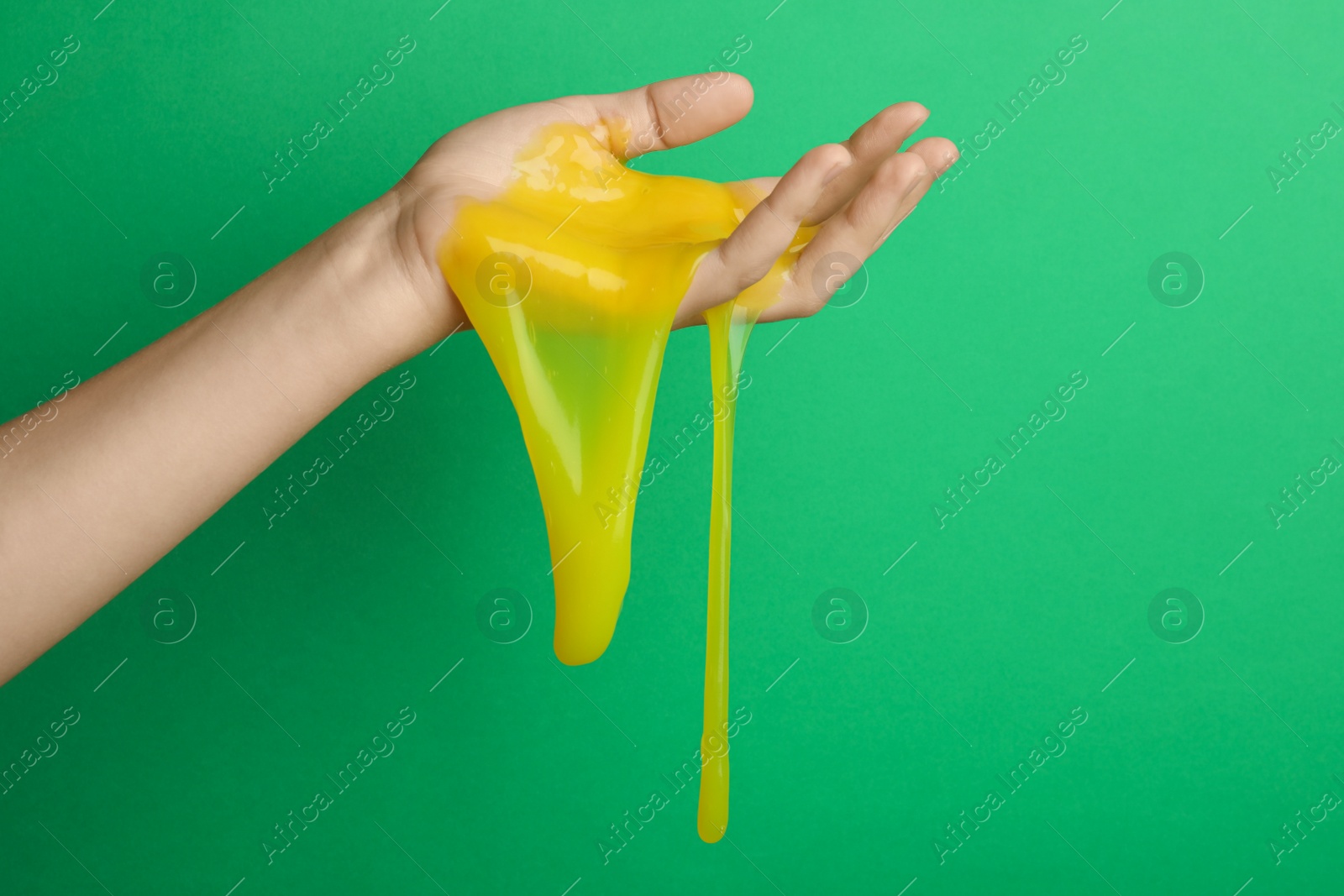 Photo of Woman playing with yellow slime on green background, closeup. Antistress toy