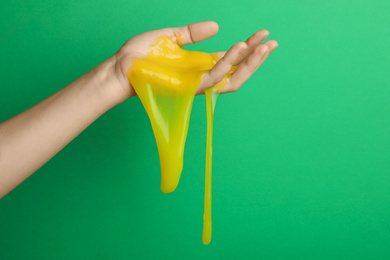 Woman playing with yellow slime on green background, closeup. Antistress toy