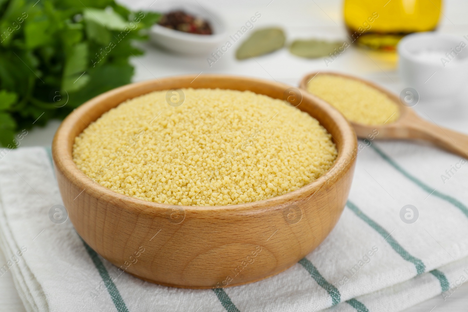 Photo of Bowl of raw couscous on white wooden table, closeup