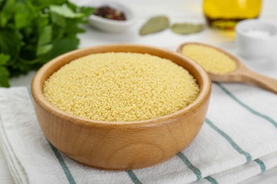 Photo of Bowl of raw couscous on white wooden table, closeup