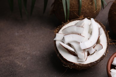 Photo of Coconut pieces in nut shell on brown table, space for text