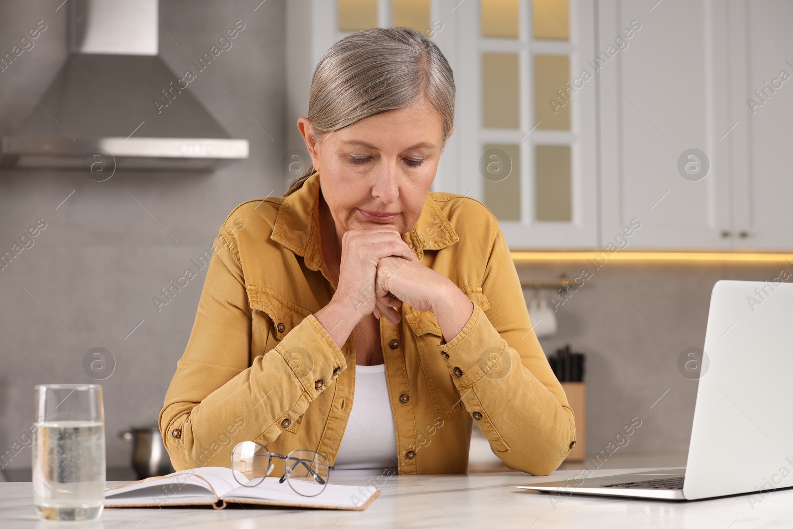 Photo of Menopause, mood changes. Sad woman at table in kitchen