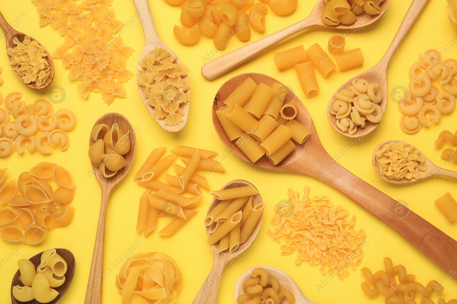 Photo of Different types of pasta on yellow background, flat lay