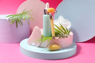 Photo of Beautiful composition with gua sha stone, face roller and bottle of serum on pink background
