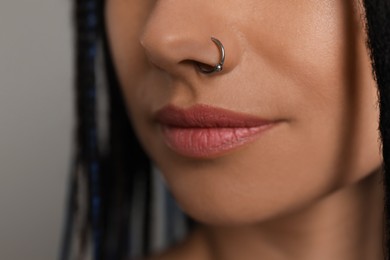 Photo of Young woman with nose piercing on grey background, closeup
