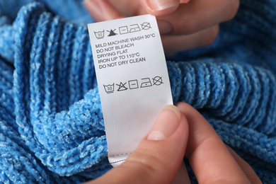 Photo of Woman reading clothing label with care symbols on blue knitted sweater, closeup