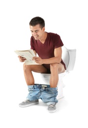 Photo of Young man reading newspaper while sitting on toilet bowl. Isolated on white