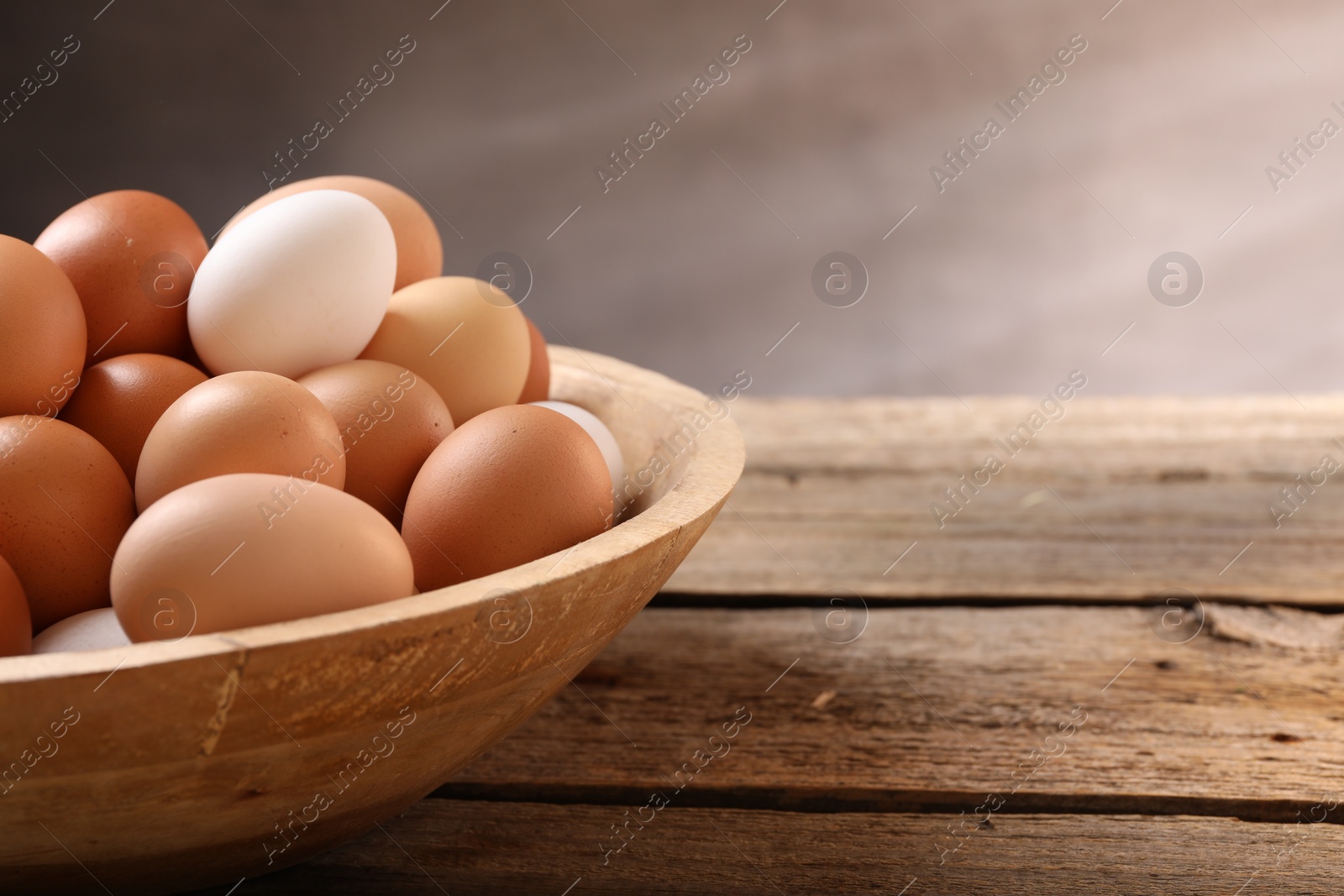 Photo of Chicken eggs in bowl on wooden table, closeup. Space for text