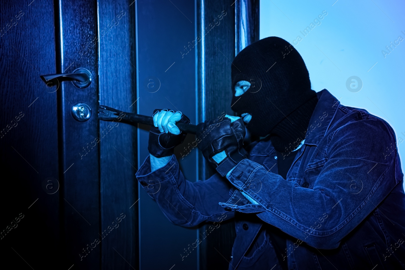 Photo of Man in mask forcing door with crow bar. Dangerous criminal