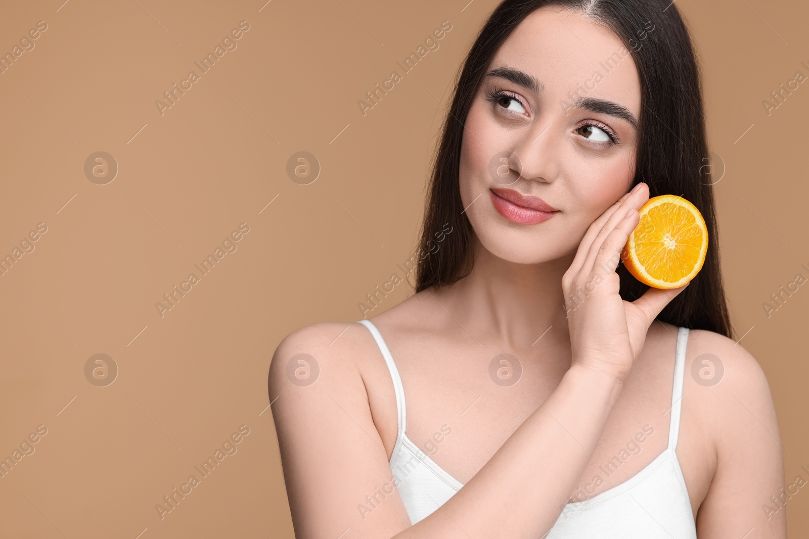 Photo of Beautiful young woman with piece of orange on beige background. Space for text