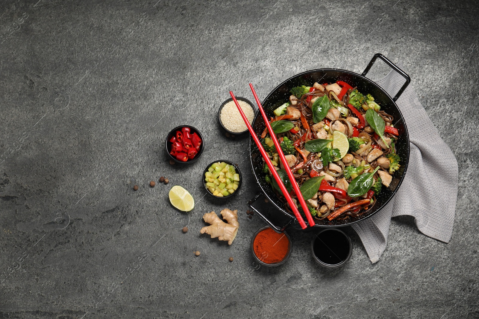 Photo of Stir-fry. Tasty noodles with meat in wok, chopsticks and ingredients on grey textured table, flat lay. Space for text