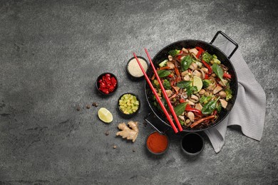 Stir-fry. Tasty noodles with meat in wok, chopsticks and ingredients on grey textured table, flat lay. Space for text