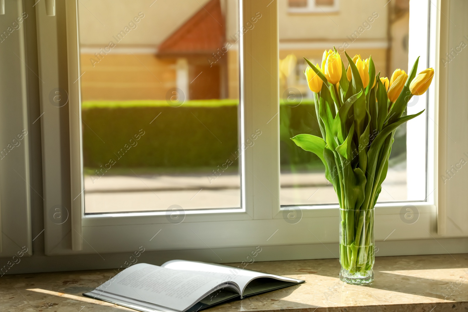 Photo of Bouquet of beautiful yellow tulip flowers in glass vase and open book on windowsill. Space for text