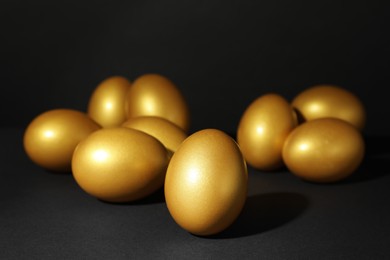 Photo of Many shiny golden eggs on black background