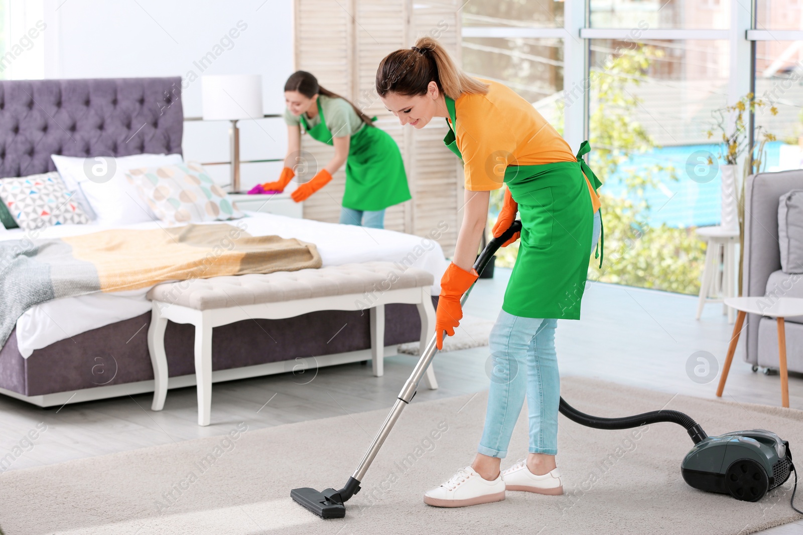 Photo of Team of professional janitors in uniform cleaning bedroom