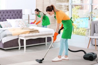 Photo of Team of professional janitors in uniform cleaning bedroom