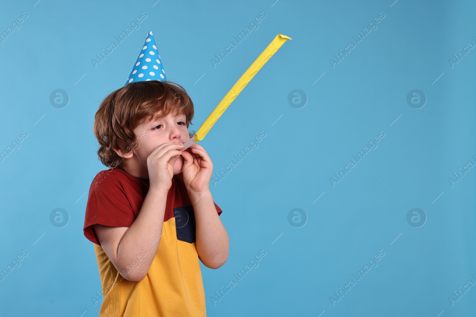 Photo of Birthday celebration. Cute little boy in party hat with blower on light blue background, space for text