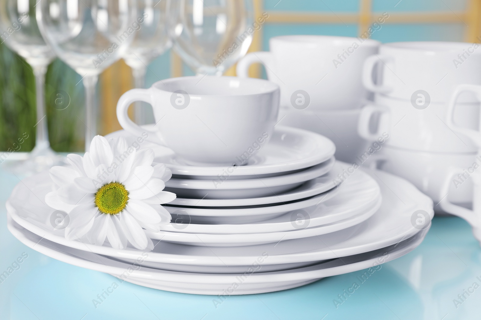 Photo of Set of clean dishware and flower on light blue table, closeup