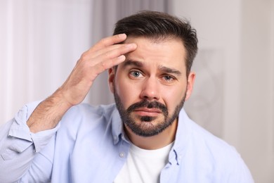 Photo of Skin problem. Confused man touching his face indoors