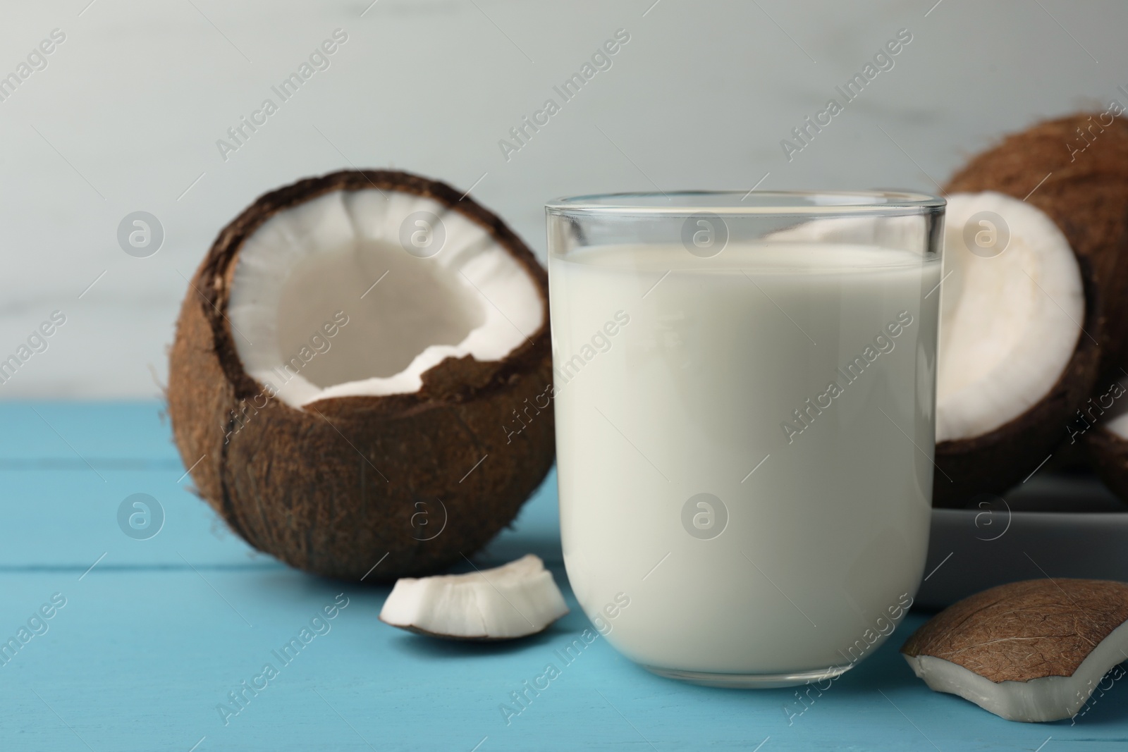 Photo of Glass of delicious vegan milk and coconuts on light blue wooden table