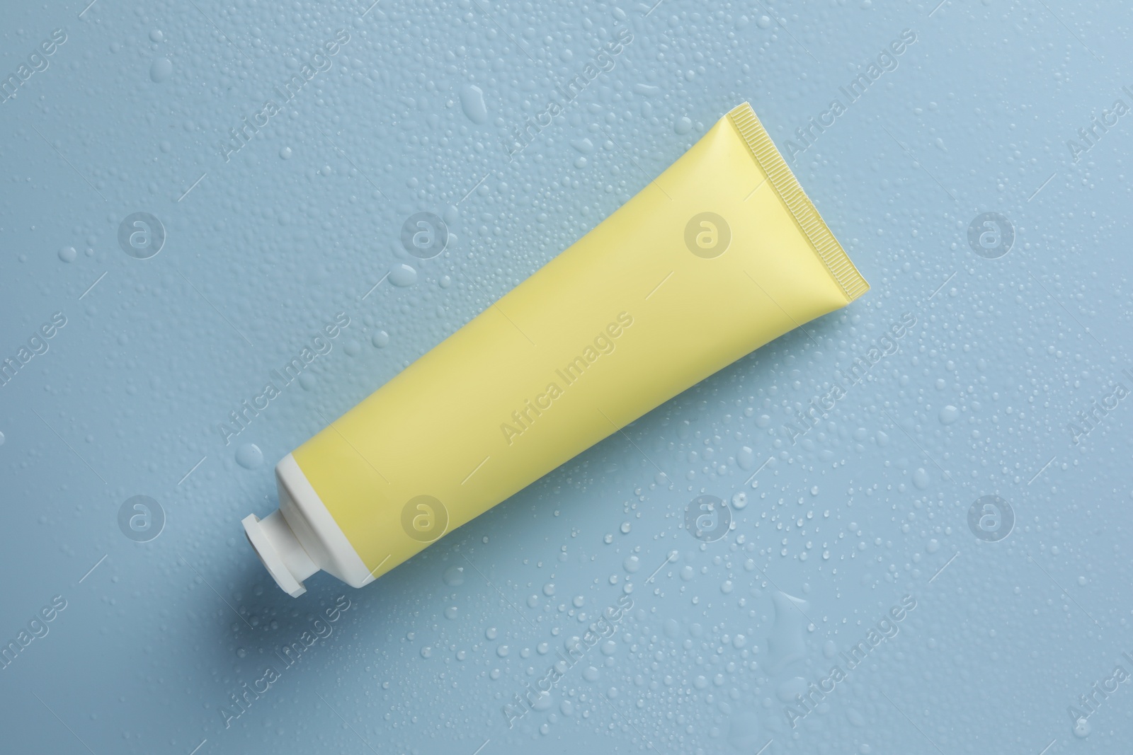 Photo of Moisturizing cream in tube on light blue background with water drops, top view