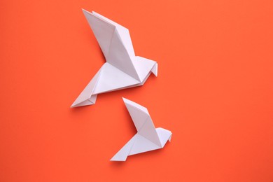 Photo of Beautiful white origami birds on orange background, flat lay