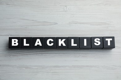 Photo of Black cubes with word Blacklist on white wooden background, flat lay